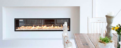 Escea DX1500 Indoor fireplace (Gas) with stones built into a white wall next to a wooden kitchen table