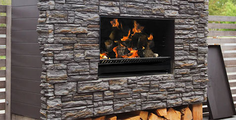 ESCEA E5000_wood outdoor fireplace built into a brown brick wall that is open to expose flames