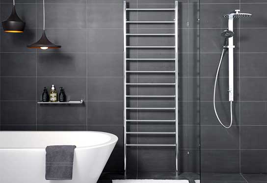 straight chrome towel rack hydronic heater against black tiles in a bathroom next to the shower and bath